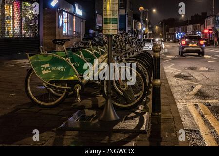 Geparkte Reihe von Leihfahrrädern in einer Vorstadtstraße in Cardiff, Wales bei Nacht Stockfoto