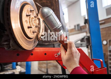 Ein Automechaniker inspiziert Bremsscheiben und Bremsbeläge mit einer Taschenlampe. Auto auf einem Reparaturständer. Technische Servicestation für Auto. Stockfoto