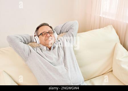 Technologie-, Menschen- und Lifestyle-Konzept – glücklicher Seniorenmann mit Kopfhörern, der zu Hause Musik hört Stockfoto