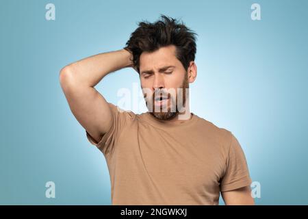 Ein müder und sehr schläfriger Mann mittleren Alters, der Hand an Kopf hält und gähnt, über blauem Studiohintergrund steht, freier Platz Stockfoto