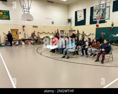 Community-Mitglieder teilen ein traditionelles Inupiaq-Lied mit Freiwilligen, die die Operation Santa Claus an der Trapper School in Nuiqsut, Alaska, unterstützen. 29. November 2022. Die Operation Santa Claus ist das alljährliche Programm der Alaska National Guard für die Zusammenarbeit und Unterstützung der Gemeinschaft, das Kindern in entlegenen Gemeinden im ganzen Bundesstaat Geschenke überreicht. In Zusammenarbeit mit der Heilsarmee lieferten der Weihnachtsmann, Frau Claus und mehr als drei Dutzend Elfen 1.420 Pfund Geschenke, Rucksäcke, Hygieneartikel und Bücher an 191 Kinder in Nuiqsut. (Alaska National Guard Foto von 1. LT. Balinda O’Neal) Stockfoto
