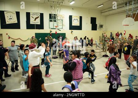 Community-Mitglieder teilen ein traditionelles Inupiaq-Lied und Tanz mit Freiwilligen, die die Operation Santa Claus an der Trapper School in Nuiqsut, Alaska, unterstützen. 29. November 2022. Die Operation Santa Claus ist das alljährliche Programm der Alaska National Guard für die Zusammenarbeit und Unterstützung der Gemeinschaft, das Kindern in entlegenen Gemeinden im ganzen Bundesstaat Geschenke überreicht. In Zusammenarbeit mit der Heilsarmee lieferten der Weihnachtsmann, Frau Claus und mehr als drei Dutzend Elfen 1.420 Pfund Geschenke, Rucksäcke, Hygieneartikel und Bücher an 191 Kinder in Nuiqsut. Stockfoto