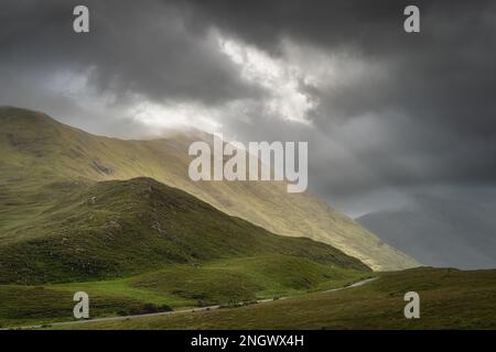 Doolough Valley, Glenummera und Glencullin Bergketten, beleuchtet von Sonnenlicht und teilweise bedeckt von dunklen Wolken, County Mayo, Irland Stockfoto