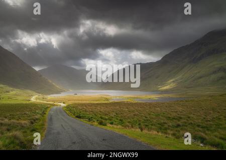 Die Straße führt durch das Doolough Valley mit Seen, zwischen Glenummera und Glencullin Gebirgsketten mit dunklem dramatischen Himmel, Mayo, Irland Stockfoto