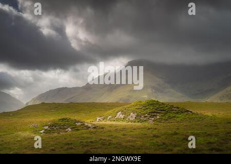 Doolough Valley, Glenummera und Glencullin Bergketten, beleuchtet von Sonnenlicht und teilweise bedeckt von dunklen Wolken, County Mayo, Irland Stockfoto