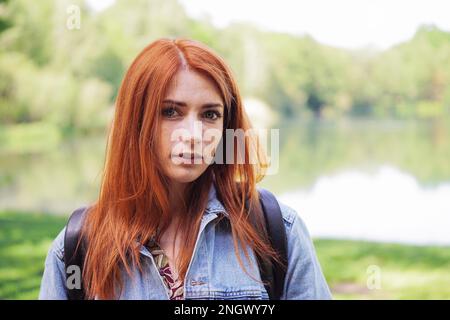 Authentische junge Frau das Tragen von Jeans Jacke und Rucksack im Freien auf einer Wanderung - reale Person stehen, See Stockfoto