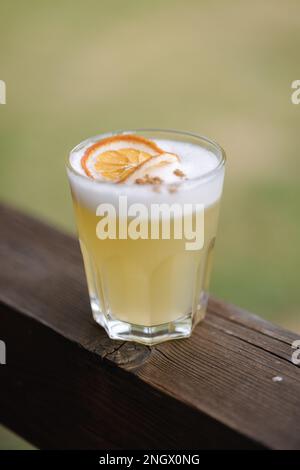 Frischer Yeallow-Gin mit Tonic und Saft. Dekoriert mit einer Scheibe getrockneter Orande und Zimtpulver. Holztisch Stockfoto