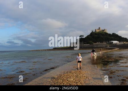 Ein Familienspaziergang entlang des leicht überdachten Fußwegs abseits von St. Michael's Mount, einer Gezeiteninsel in Mount's Bay, Cornwall, bevor sie vollständig bedeckt ist Stockfoto