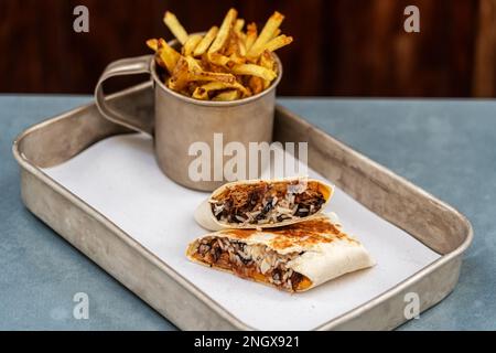 Wickeln Sie einen Schweinehühnchen-Burrito mit Gewürzen und Pommes frites in eine Tasse. Holzhintergrund Stockfoto