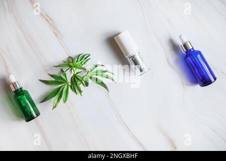 Kosmetikpaket. Cremefarbene Tube- und Bodylotion-Verpackung Kosmetikpackung auf hellem Marmorhintergrund neben frischen Marihuana-Blättern. Stockfoto