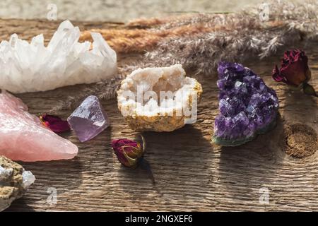 Mehrere Edelsteine für esoterische spirituelle Übungen oder Zauberkunst auf einem Holztisch mit trockenen Kräutern und Blumen. Sammlung von Steinen und Mineralien. Stockfoto