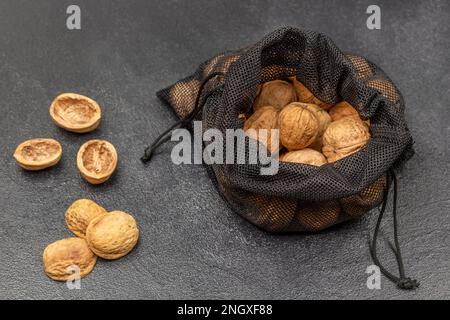 Walnüsse in einem schwarzen, wiederverwendbaren Beutel. Mutternschalen auf dem Tisch. Draufsicht. Schwarzer Hintergrund. Stockfoto