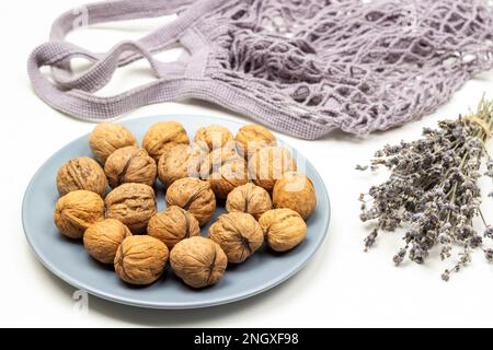 Ganze Walnüsse auf einem blauen Teller. Ein Strauß trockener Lavendelzweige. Gewebebeutel. Draufsicht. Weißer Hintergrund Stockfoto