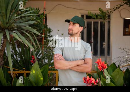 Nahaufnahme Porträt Mann mittleren Alters, der im Haus arbeitet, Gärtner vor blühenden roten Blumen Calathea Lutea Plant. Landschaftsdesign Stockfoto