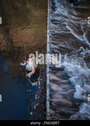 Die Kinderpuppe hat sich in einem Metalleinzugsgebiet in einem schnell fließenden Fluss verfangen. Stockfoto