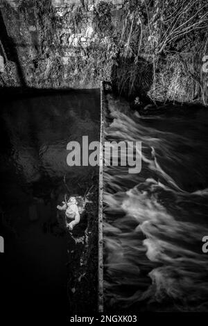 Die Kinderpuppe hat sich in einem Metalleinzugsgebiet in einem schnell fließenden Fluss verfangen. Stockfoto