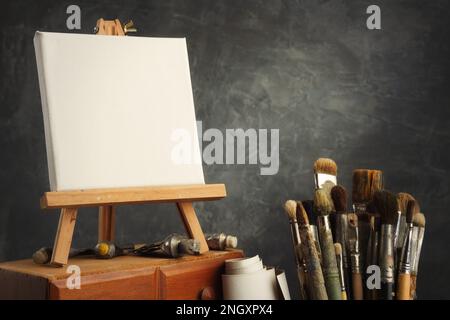 Künstlerische Ausstattung in einem Künstlerstudio: Leere Leinwand auf einer Staffelei aus Holz, Farbrohre und Pinsel - benutzte künstlerische Pinsel zum Malen Stockfoto