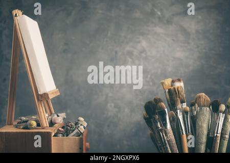 Künstlerische Ausstattung in einem Künstlerstudio: Leinwand eines Künstlers auf einer Staffelei aus Holz, Farbrohre und Pinsel - benutzte künstlerische Pinsel zum Malen Stockfoto