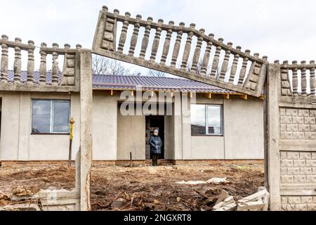 Bucha, Oblast Kiew, Ukraine. 18. Februar 2023. Eine Assistenzärztin steht vor ihrem renovierten Haus, das vor einem Jahr in der Vokzalna-Straße bombardiert wurde. Die Frau blieb während der Schlacht im März 2022 in Bucha, sie versteckte sich in örtlichen Schulunterkünften. Während sich die Invasion der Ukraine durch die russischen Streitkräfte ihrem ersten Jahrestag nähert, sammeln die Bewohner von Bucha Geld, um ihre Häuser wieder aufzubauen. Die meisten Bewohner der Vokzalna-Straße, eine der am meisten zerstörten Straßen während des Kampfes um Kiew im März 2022, haben jetzt die Möglichkeit, ihre Häuser wieder aufzubauen oder zu renovieren. Es gibt andere Teile von B. Stockfoto