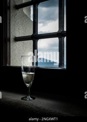 Ein Glas Champagner in einem alten, verschließbaren Burgfenster mit Blick auf die Berge, den bewaldeten Himmel Stockfoto