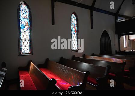 Sonnenlicht strömt durch Buntglasfenster auf Bänke in der Holy Trinity Episcopal Church, die 1850 im ländlichen Hertford, North Carolina, fertiggestellt wurde. Stockfoto