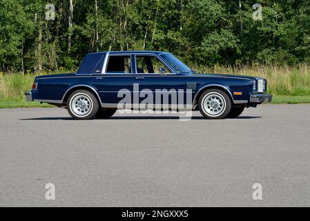 Ein dunkelblauer Chrysler New Yorker Fifth Avenue Edition aus dem Jahr 1982 bietet einen breiten Blick auf Bäume in der hellen Sonne. Stockfoto