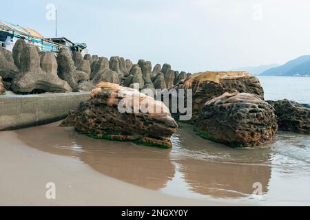 Sandstrand auf bewölktem Hintergrund. Es gibt Dolos Blöcke, um Wellen zu vermeiden. Stockfoto