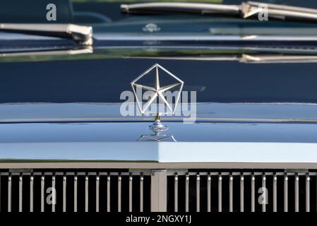 Die Pentastar-Haube über dem Kühlergrill auf einem dunkelblauen Chrysler New Yorker Fifth Avenue Edition aus dem Jahr 1982 in heller Sonne. Stockfoto