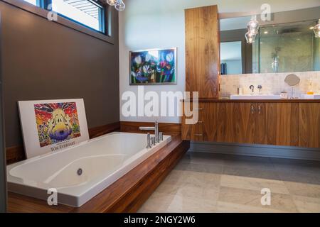 Waschtisch und Sockel aus Walnussholz mit tiefweißer Acrylbadewanne im Bad mit grauem und weißem Marmorboden in einem luxuriösen, modernen Haus. Stockfoto