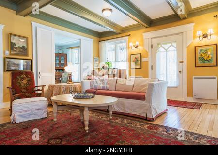 Sofabett aus rotem Samt, gepolsterter Holzsessel, weißer Holztisch im Wohnzimmer mit rotem Teppich und Birkenholzböden. Stockfoto