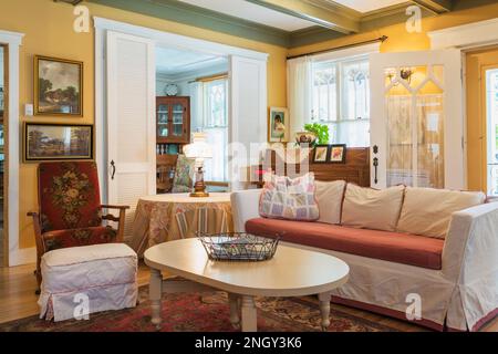 Sofabett aus rotem Samt, gepolsterter Holzsessel, weißer Holztisch im Wohnzimmer mit rotem Teppich und Birkenholzböden. Stockfoto