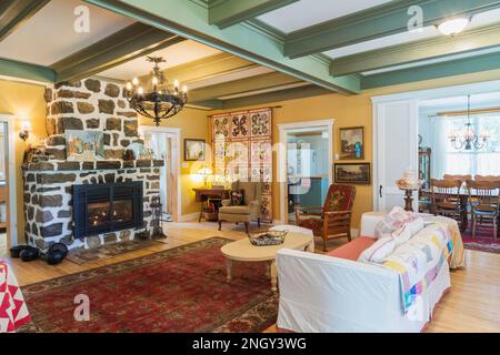 Sofabett aus rotem Samt, gepolsterte Sessel aus Holz, weißer gemalter Kaffeetisch aus Holz, Gaskamin aus Naturstein im Wohnzimmer des 1920er. Hauses. Stockfoto