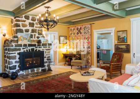 Sofabett aus rotem Samt, gepolsterte Sessel aus Holz, weißer gemalter Kaffeetisch aus Holz, Gaskamin aus Naturstein im Wohnzimmer des 1920er. Hauses. Stockfoto