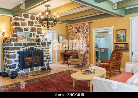 Sofabett aus rotem Samt, gepolsterte Sessel aus Holz, weißer gemalter Kaffeetisch aus Holz, Gaskamin aus Naturstein im Wohnzimmer des 1920er. Hauses. Stockfoto