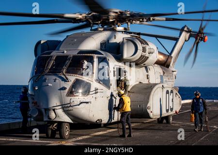 USA Navy-Matrosen, die dem Amphibien-Transportschiff USS Arlington (LPD 24) der San Antonio-Klasse zugewiesen sind, entfernen während des Flugbetriebs an Bord von Arlington am 14. Februar 2023 Keile und Ketten von einem Sikorsky CH-53K King Hallion Helikopter. Der King Hallion ist ein schwerer Frachthubschrauber, der als nächste Weiterentwicklung der seit 1966 in Betrieb befindlichen Hubschrauber der CH-53-Serie Seetests unterzogen wird. (USA Marinebild von Mass Communication Specialist 1. Klasse John Bellino) Stockfoto