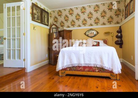 1930er Doppelbett mit Kopfteil aus Kiefernholz, weiße Bettüberwürfe, antike Ahornapotheke aus Noppen-Ahornholz, Buntböden aus geöltem Kiefernholz. Stockfoto