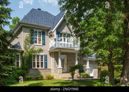 Hellbraune Backsteine und Vinyl verkleidete Landhausfassade im Landhausstil mit weißen und blauen Zierleisten im Sommer. Stockfoto