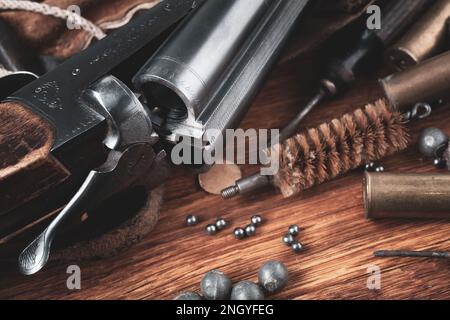 Antike 16-Gauge Break-Action glatt gebohrte Schrotflinte mit Messinggehäuse und Zubehör für Patronennachladung auf Holztisch. Stockfoto