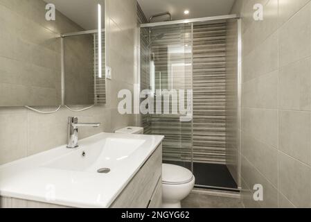 Kleines Badezimmer mit einteiligem Waschbecken aus Harz auf einem Schrank mit Schubladen, Duschkabine mit Glaskabine und Spalier-Fliesen Stockfoto