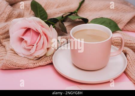 Eine Kaffeetasse und eine rosa Rose auf einem Strickpullover. Urlaubskonzept. Nahaufnahme Stockfoto