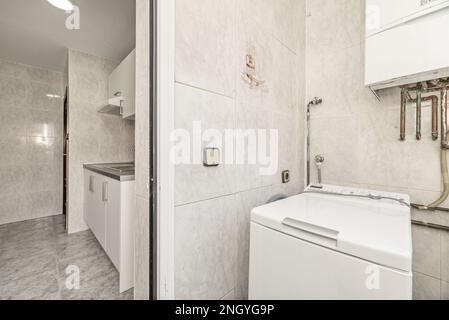 Kleine Apartmentküche mit Trockenterrasse mit Waschmaschine und Erdgaskessel, Steinzeug-Fußboden und passenden Wänden Stockfoto