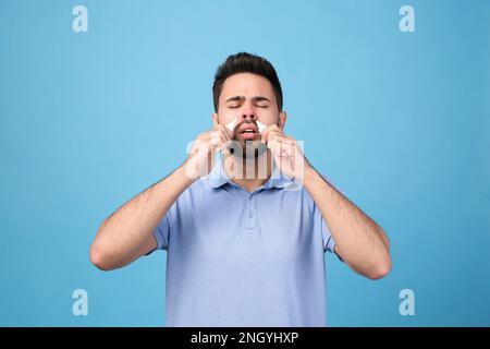 Mann mit Nasensprays auf hellblauem Hintergrund Stockfoto