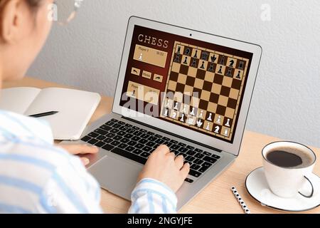 Eine Frau, die online Schach auf einem Laptop spielt, am Tisch, Nahaufnahme Stockfoto
