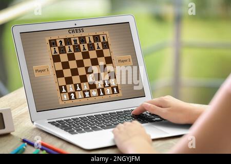 Eine Frau, die online Schach auf einem Laptop spielt, am Tisch, Nahaufnahme Stockfoto