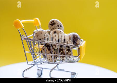 Frohe Ostergeschichte. Osterwachteleier im Einkaufswagen auf hellgelbem Papier. Festliches Konzept Stockfoto