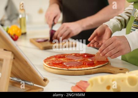 Ein Paar, das zusammen Pizza macht, während es sich einen Online-Kochkurs über ein Tablet in der Küche ansieht, Nahaufnahme Stockfoto