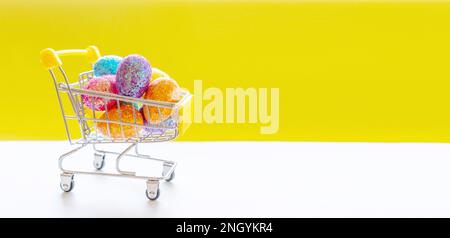 Frohe Ostergeschichte. Mehrfarbige Ostereier in einem Korb auf hellgelbem Papier. Festliches Konzept Stockfoto