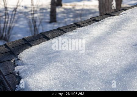 Vollformat abstrakter Texturhintergrund von Schnee, der unter natürlichem Sonnenlicht auf einem Schindeldach aus Asphalt zu schmelzen beginnt Stockfoto