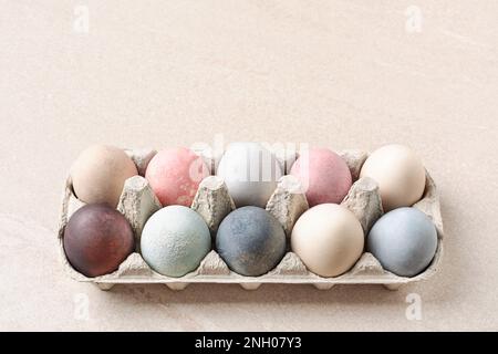 Natürlich gefärbte Ostereier in Pappschachtel auf beigefarbenem Tisch als Kopierraum. Eco-Konzept. Pastelltöne. Stockfoto