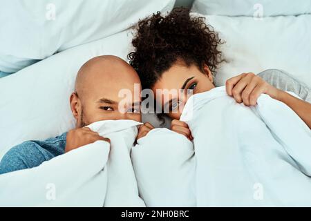 Besondere Momente unter der Abdeckung teilen. Ein liebevolles junges Paar in ihrem Schlafzimmer. Stockfoto